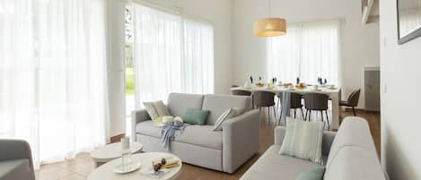 A modern living room with a sofa, a dining table set for breakfast, and a kitchen in the background.