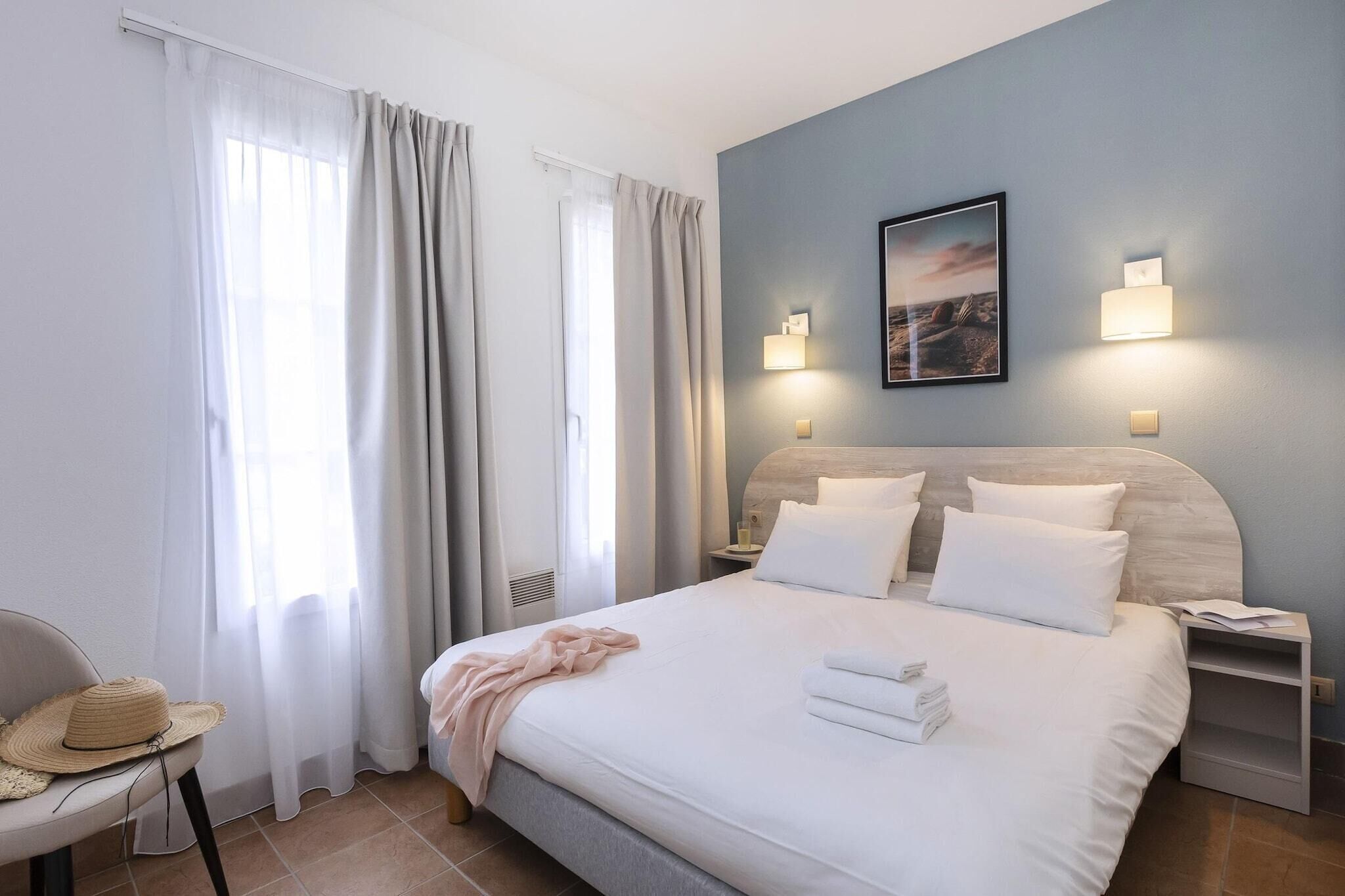 A hotel room with a bed, a chair, a nightstand, and a wall-mounted lamp.