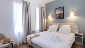 A hotel room with a bed, a chair, a nightstand, and a wall-mounted lamp. - Villa in France with Golf Course & Pool (Gujan Mestras)