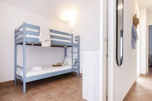 Una cama litera con una toalla blanca y un osito de peluche, un espejo en la pared y un piso de baldosas.