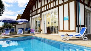 A swimming pool with lounge chairs and umbrellas, a building with large windows, and a sign indicating a restaurant or dining area. - Villa in France with Golf Course & Pool (Gujan Mestras)