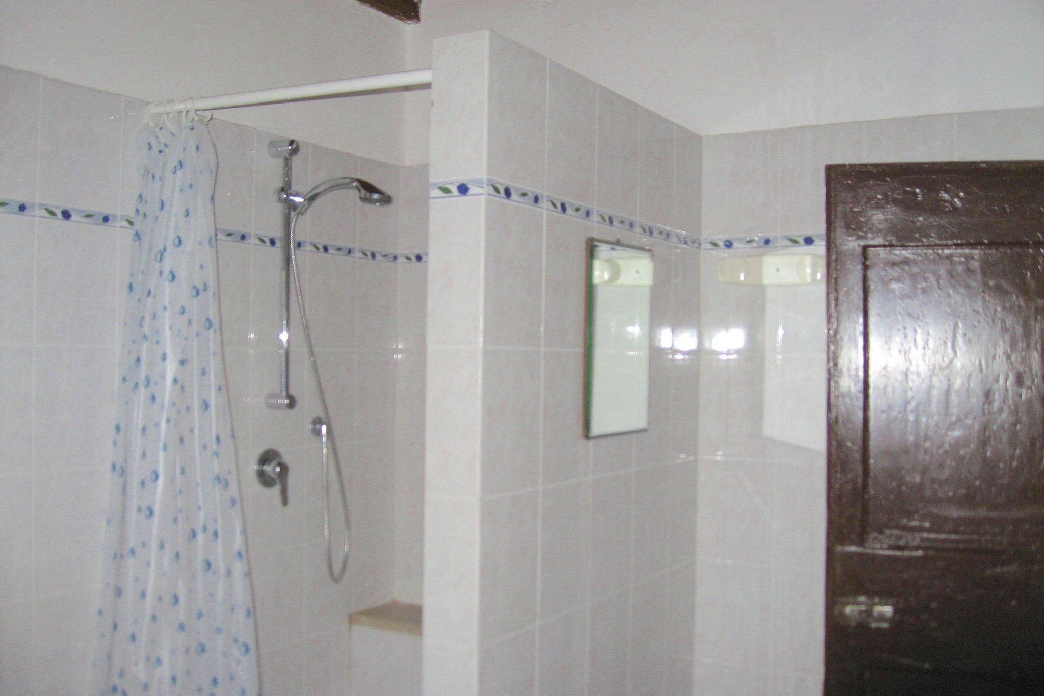 Une salle de bain avec des murs recouverts de carreaux blancs, une douche avec une porte en verre et une porte en bois.
