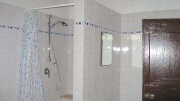 Une salle de bain avec des murs recouverts de carreaux blancs, une douche avec une porte en verre et une porte en bois.