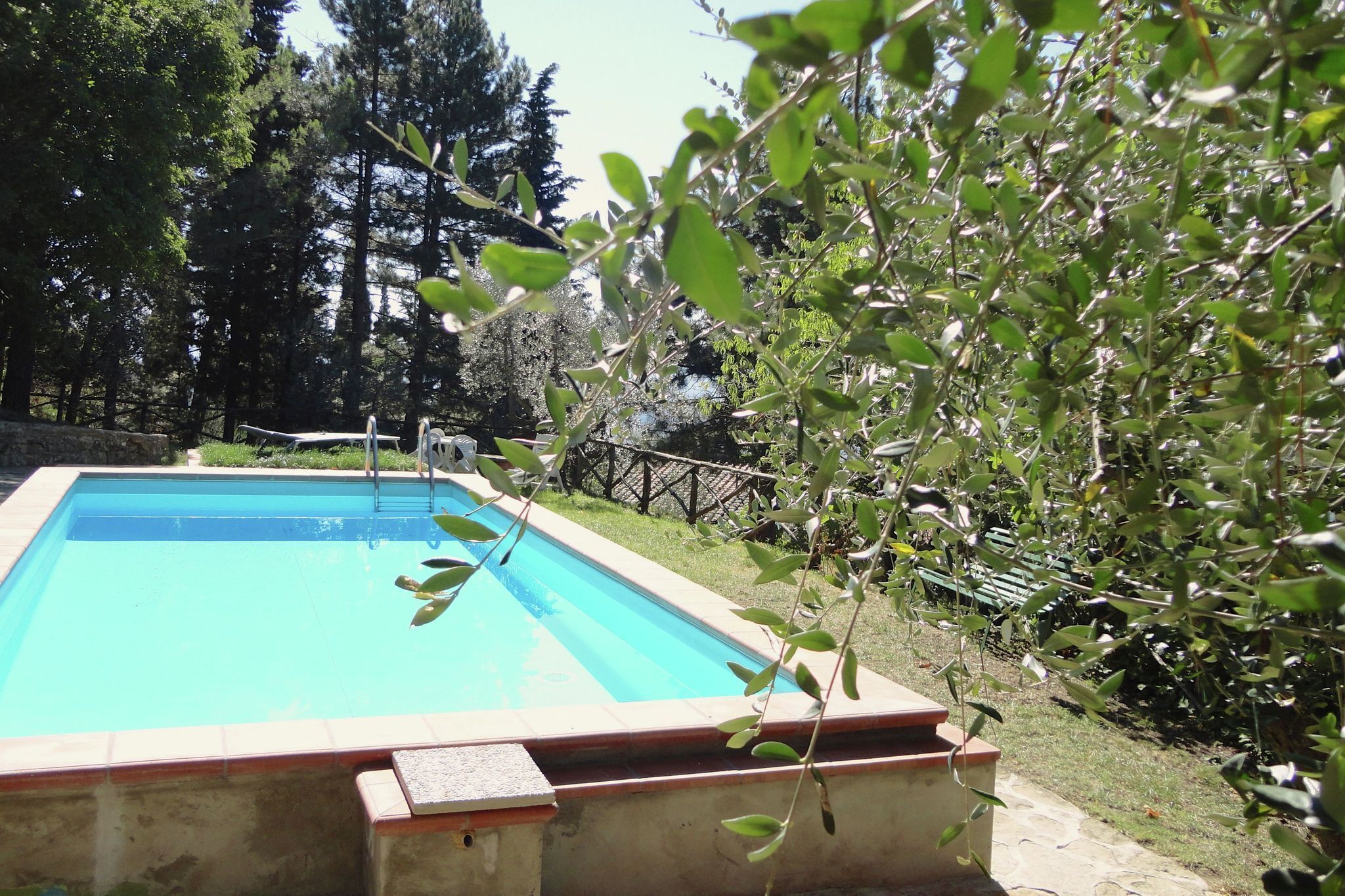 Une piscine rectangulaire dont les bords sont recouverts de carreaux, entourée d’un mur de pierre et d’une clôture en bois.
