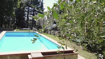 Une piscine rectangulaire dont les bords sont recouverts de carreaux, entourée d’un mur de pierre et d’une clôture en bois.