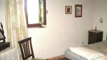 Une chambre à coucher avec un lit, une chaise, une petite table et une fenêtre avec des rideaux.