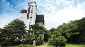 A modern building with a tower, surrounded by lush greenery and a stone pathway. - Hotel Soopil (Osan)