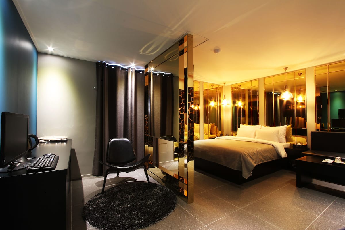 A modern hotel room with a bed, desk, chair, and a large mirror.