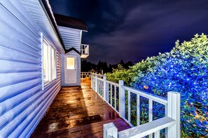 Una terraza de madera con barandilla blanca, un cobertizo pequeño y un jardín bien iluminado.