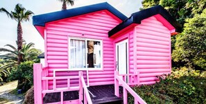 Una casa de madera rosa con techo negro, un pequeño porche y una ventana.