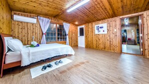 Een kamer met houten lambrisering, een bed, een raam met gordijnen, een deur en een klein tafeltje met een fotolijst.
