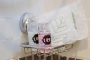 Un espace douche équipé d’une étagère en métal où sont posés deux flacons de savon liquide et un bonnet de douche.