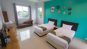 Une chambre d’hôtel avec deux lits, un canapé, un bureau et une vue sur la verdure environnante.