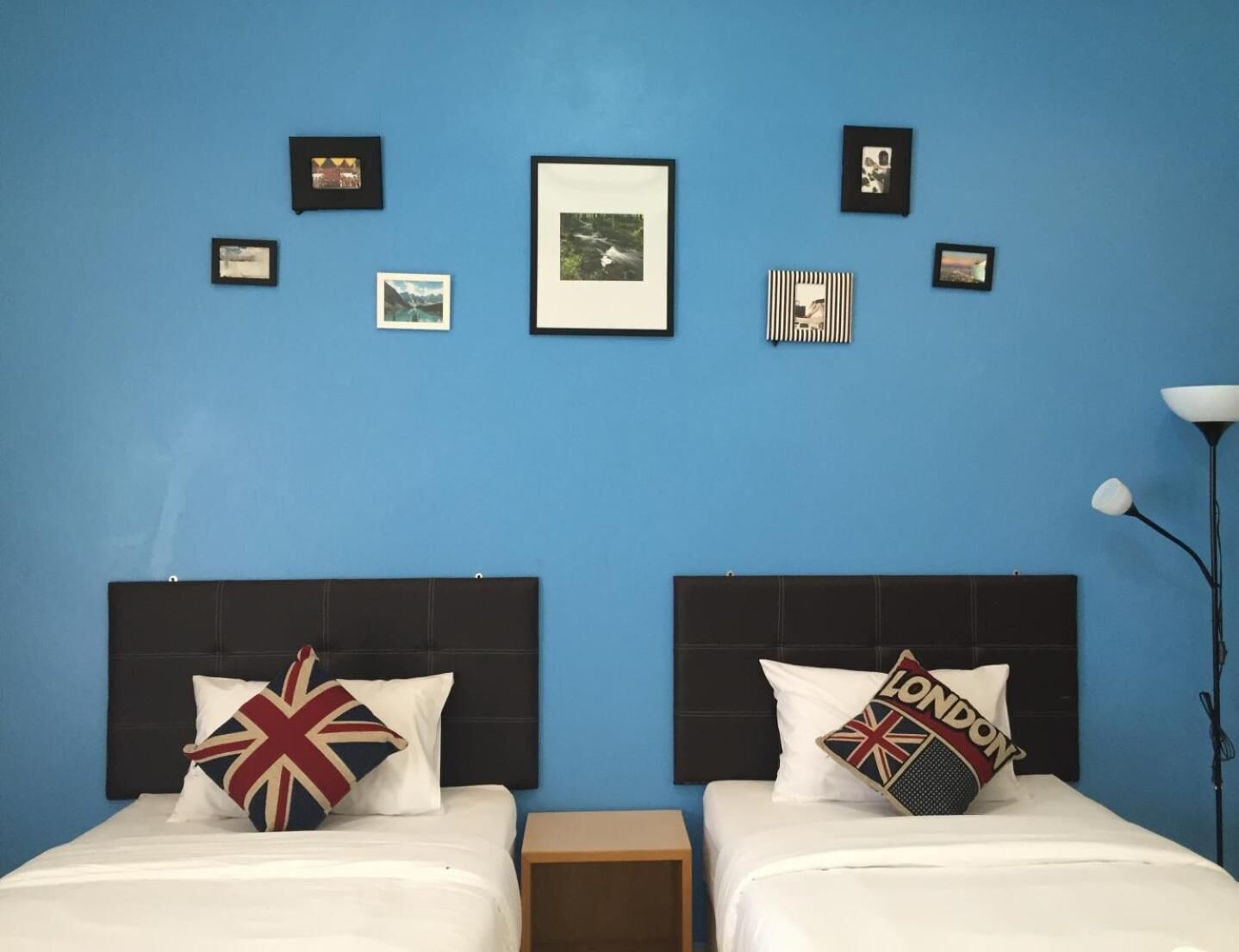 Una habitación de hotel con dos camas, pared azul, cuadros enmarcados y una lámpara.