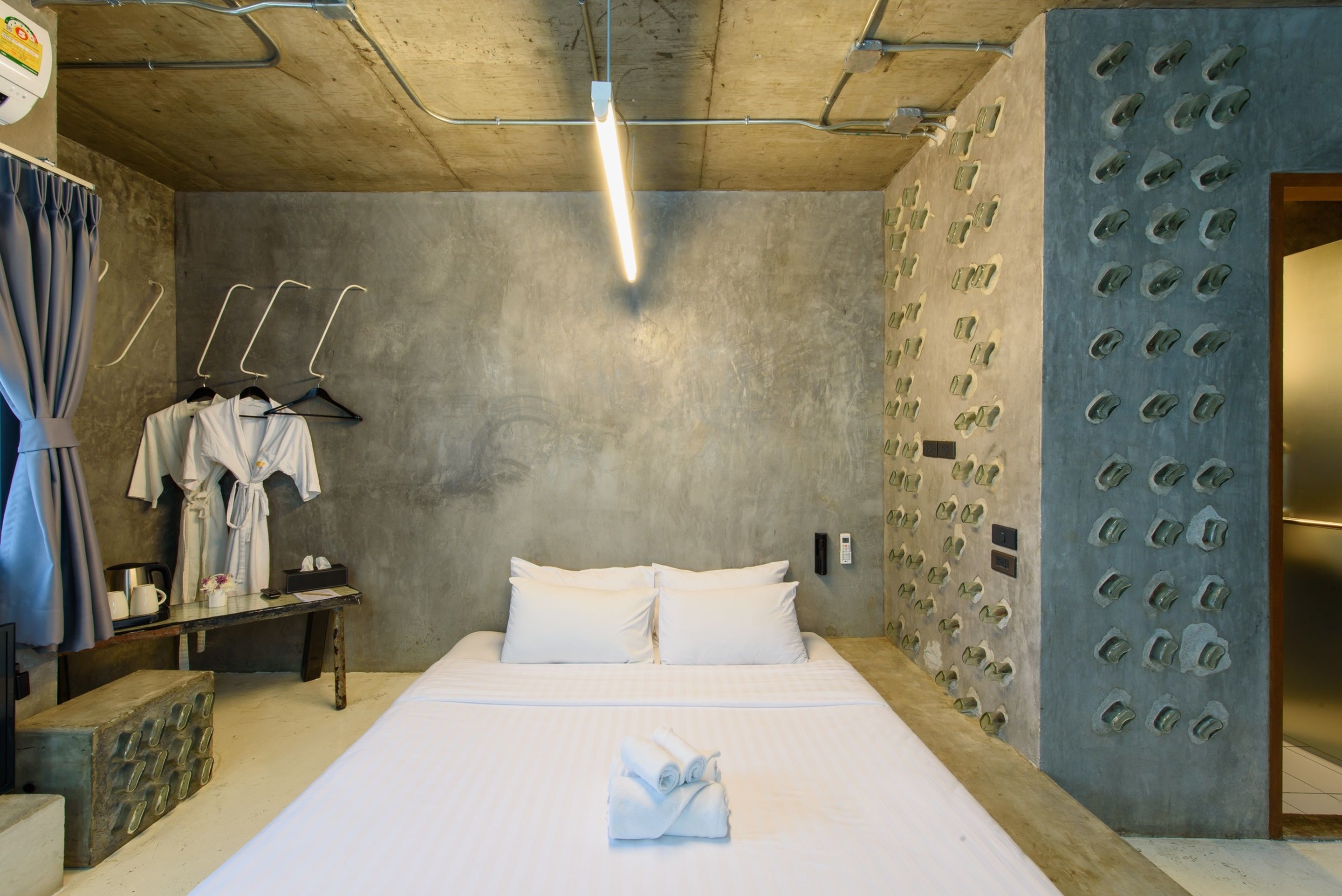 A hotel room with a large bed, a bedside table with a lamp, a wardrobe, and a wall with a unique textured design.
