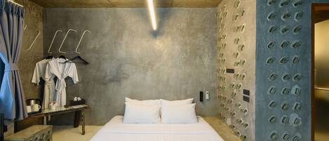 A hotel room with a large bed, a bedside table with a lamp, a wardrobe, and a wall with a unique textured design.