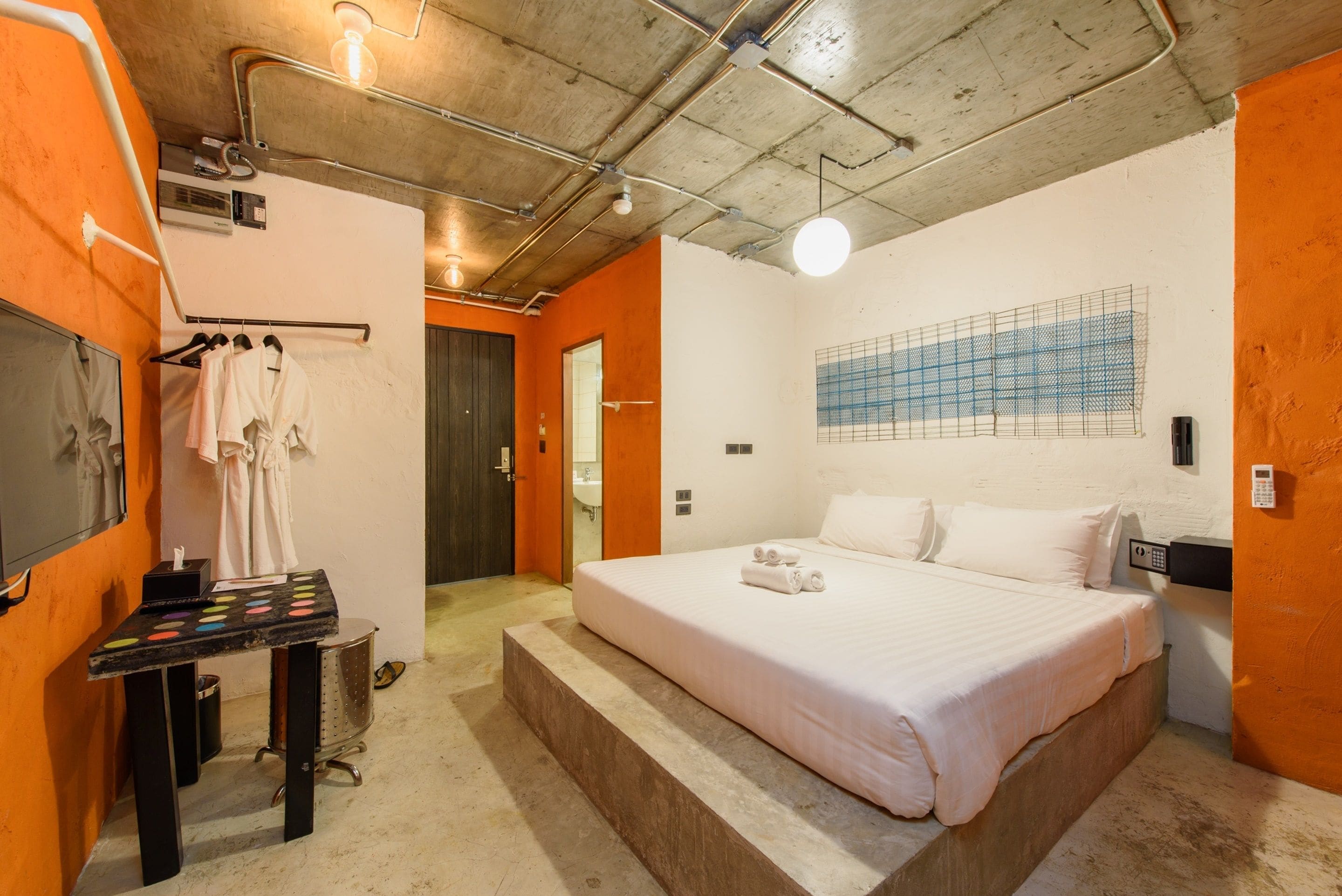 Habitación de hotel con una cama grande, una mesita con una bandeja de toallas, un espejo y un televisor montado en la pared.