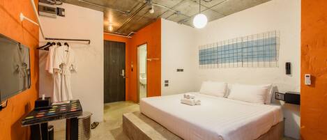 Habitación de hotel con una cama grande, una mesita con una bandeja de toallas, un espejo y un televisor montado en la pared.