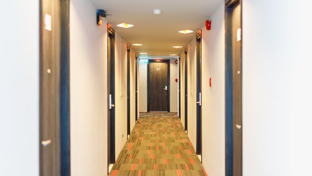Un pasillo de hotel con pisos alfombrados, puertas a ambos lados y luces en el techo.