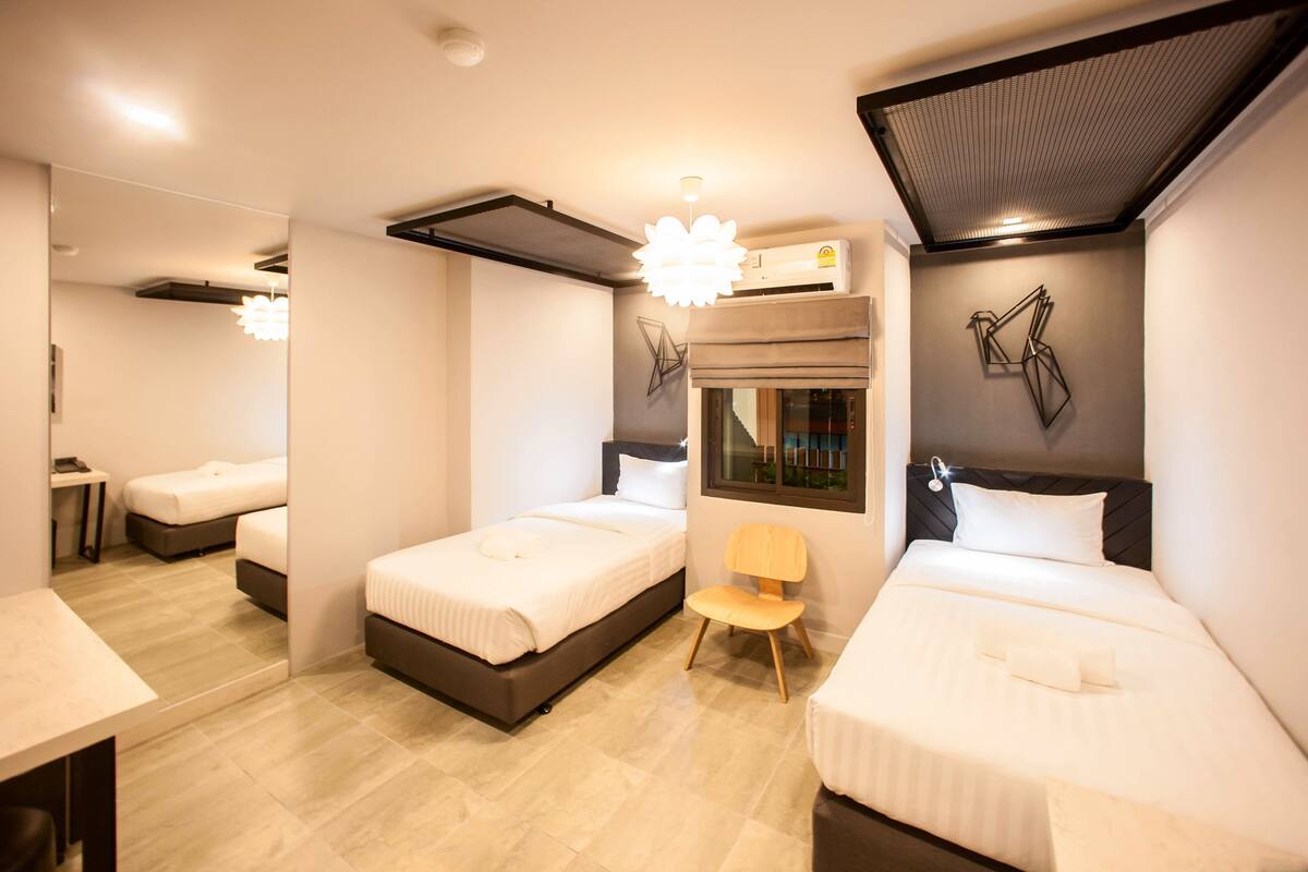 A modern hotel room with two beds, a chair, a desk, and a large mirror.