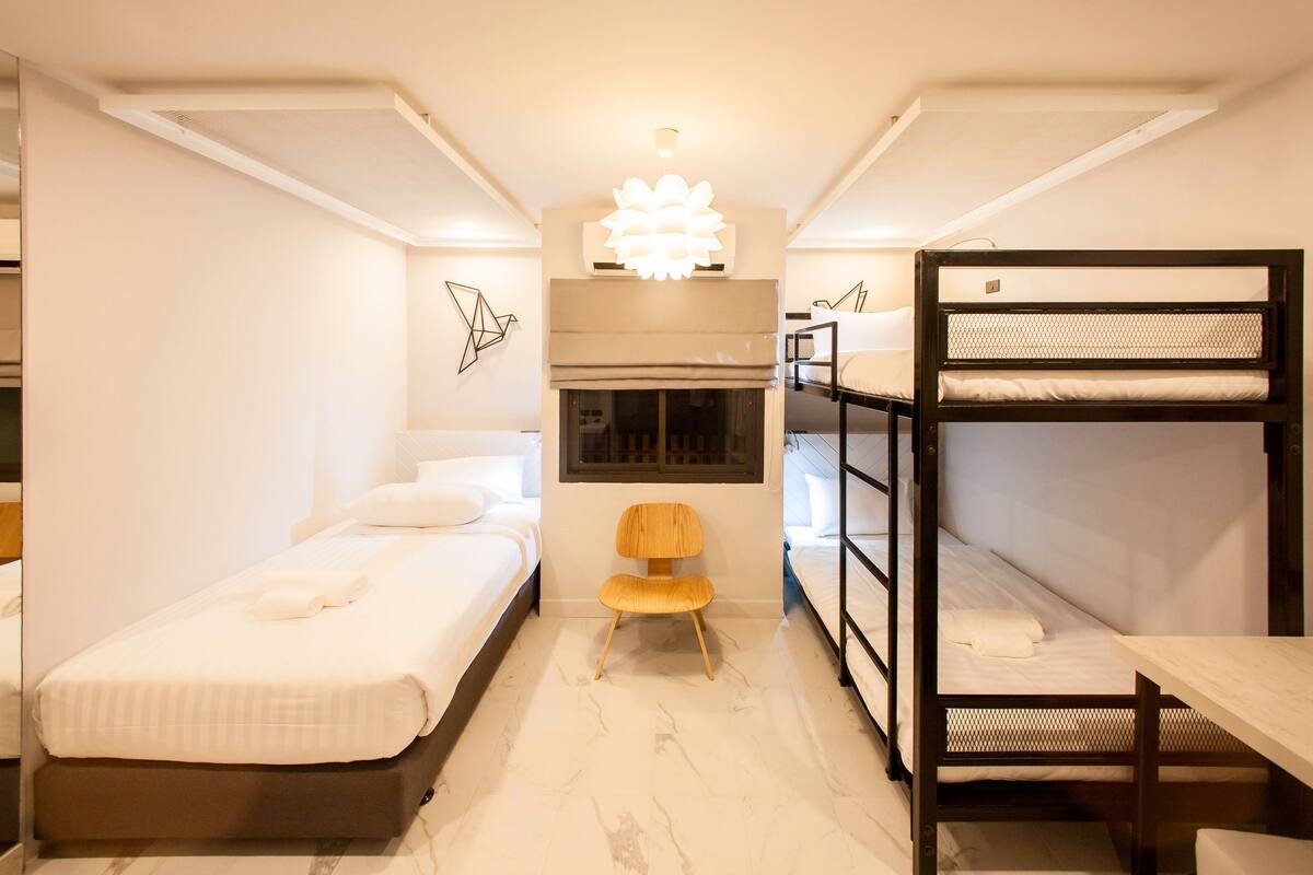 A compact hotel room with a single bed, a bunk bed, a wooden chair, and a small table.