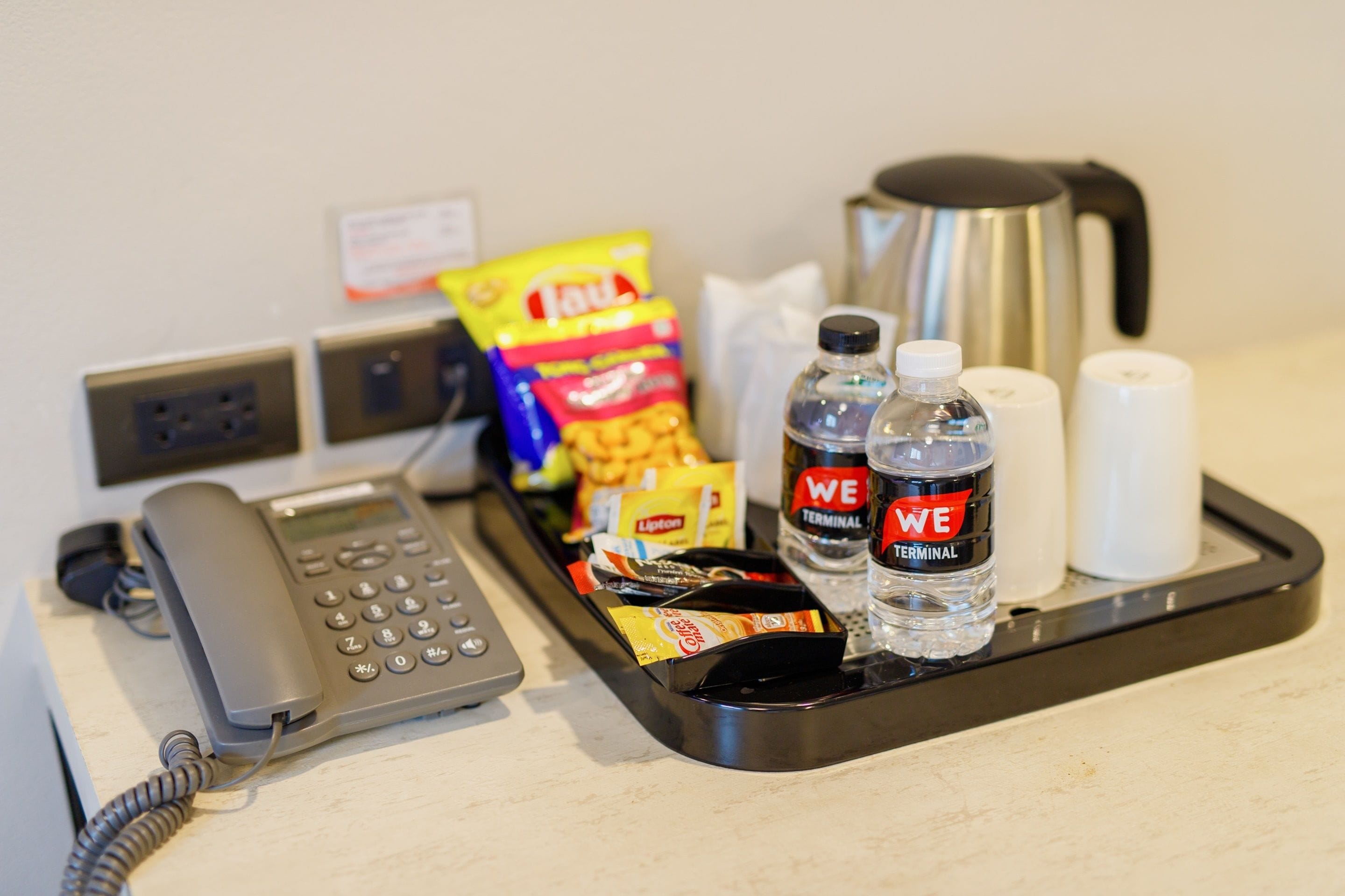 Escritorio en una habitación de hotel con teléfono fijo, una bandeja con bocadillos, agua embotellada y una cafetera.