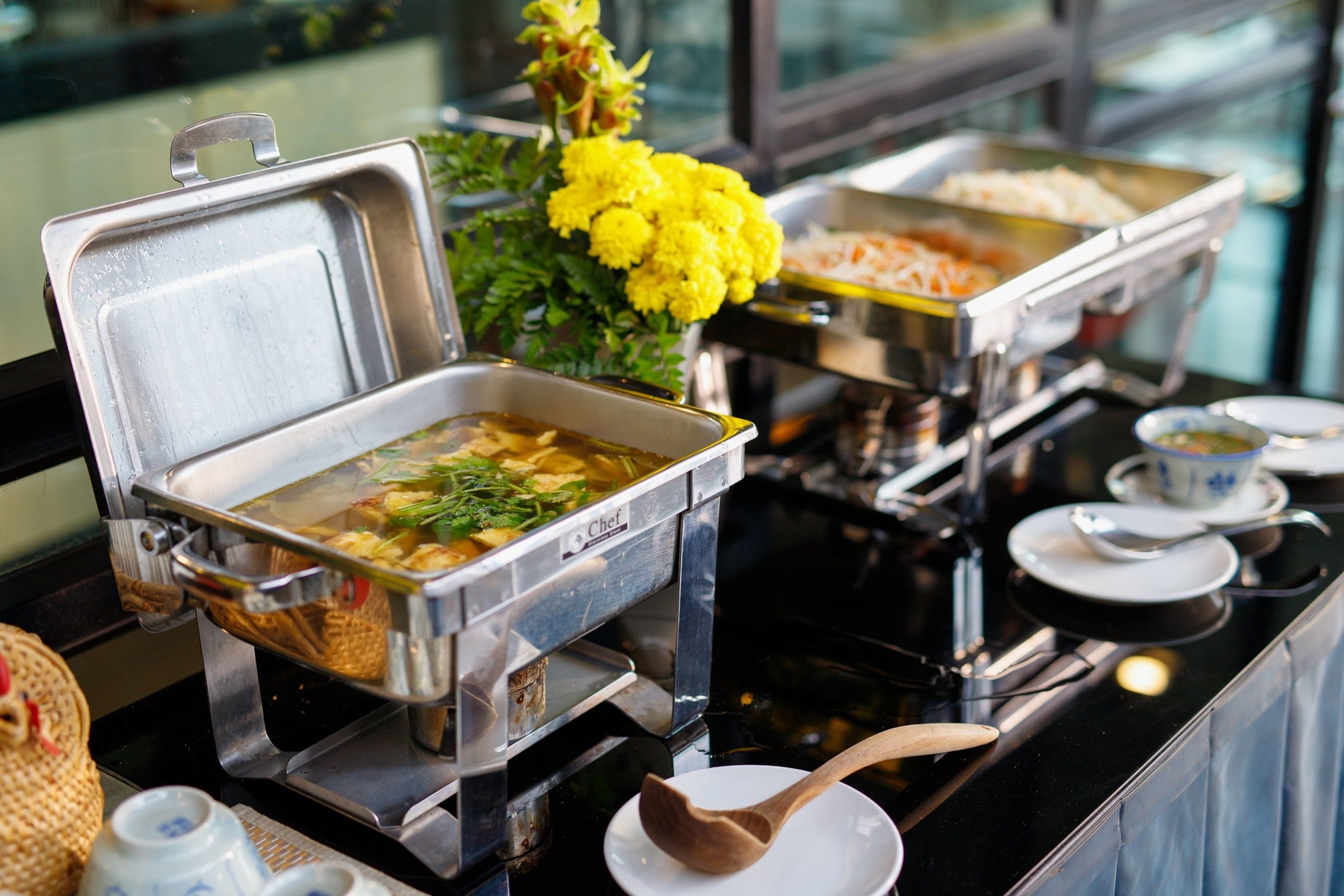 A buffet setup with various food items and a decorative yellow flower arrangement.