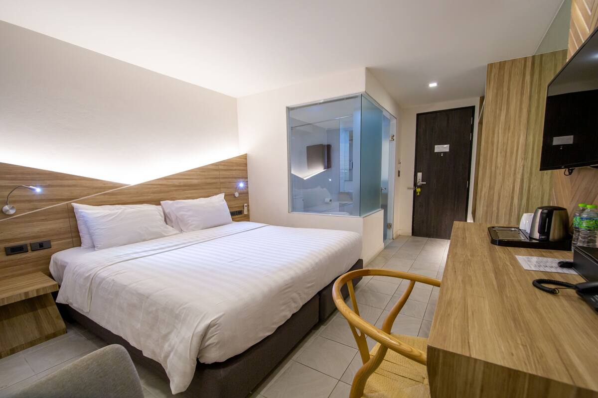 A modern hotel room with a large bed, a desk with a coffee maker, and a TV mounted on the wall.