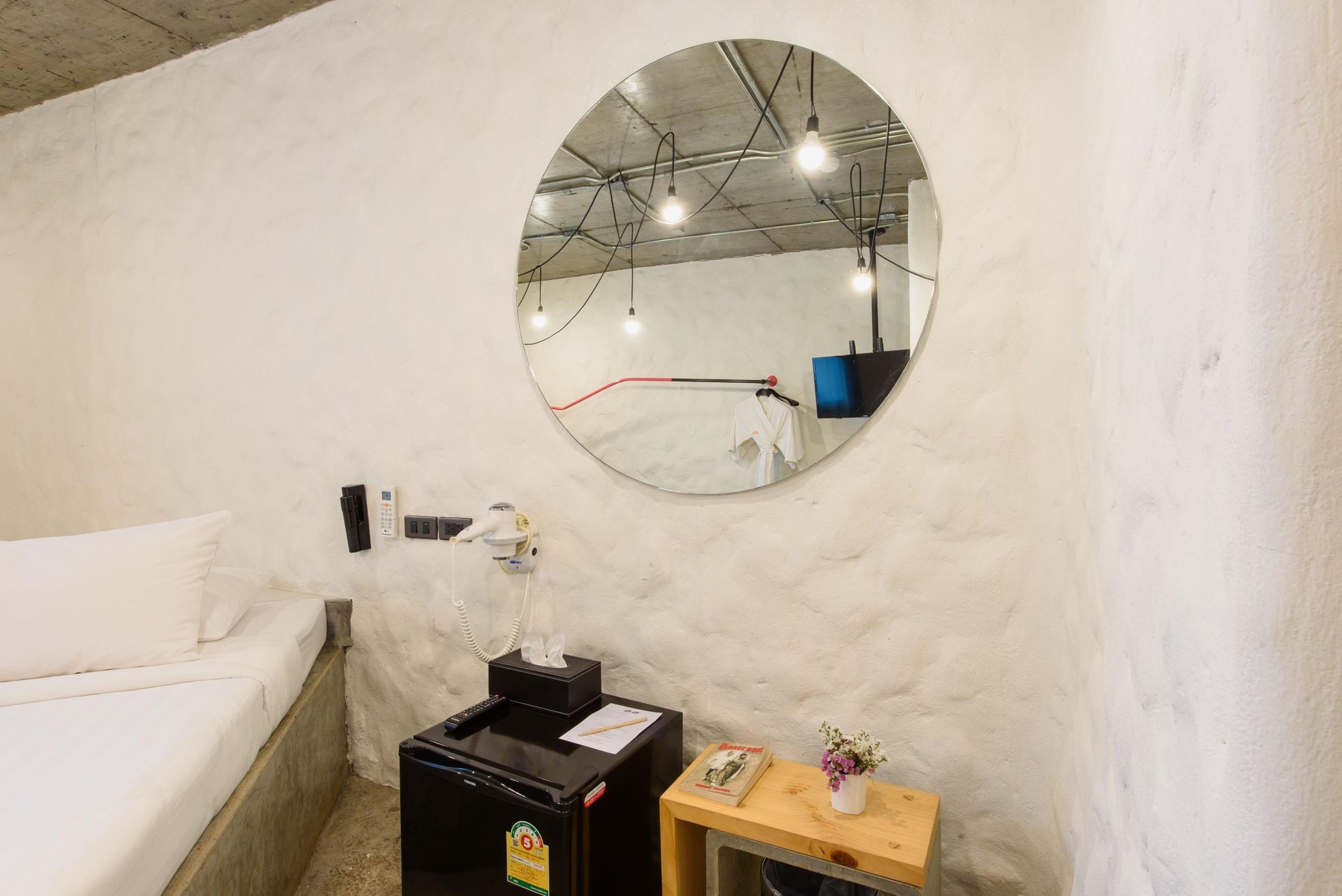 Una habitación con una cama, un espejo, una mesita con un florero y un refrigerador negro.