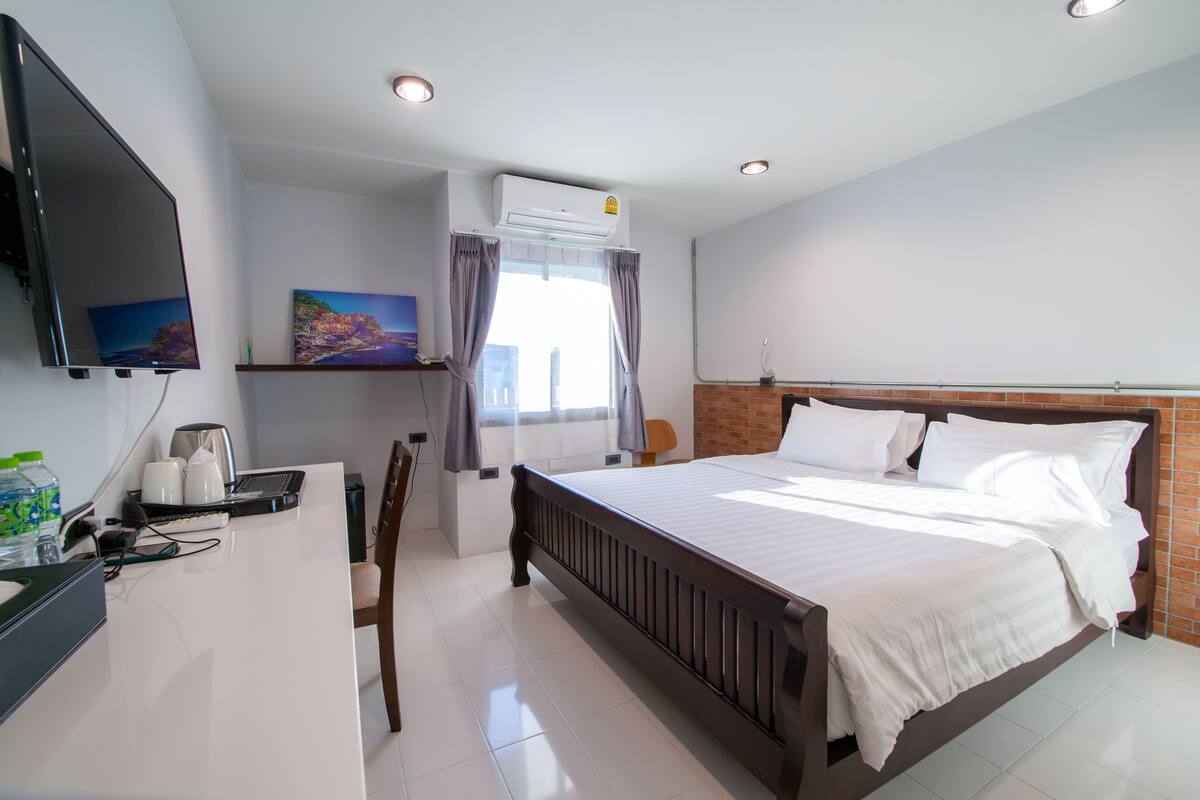 A hotel room with a bed, a desk with a computer, a TV, and a window with curtains.