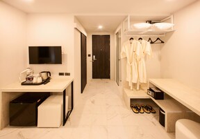 Une chambre d’hôtel moderne équipée d’une télévision à écran plat, d’un bureau avec une bouilloire et des tasses, d’un banc, d’un porte-peignoir avec des peignoirs et d’un espace pour ranger les chaussures.