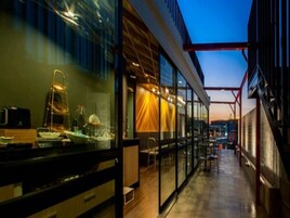 Un bâtiment moderne doté de grandes fenêtres en verre et d’un espace extérieur couvert aménagé avec des tables et des chaises.