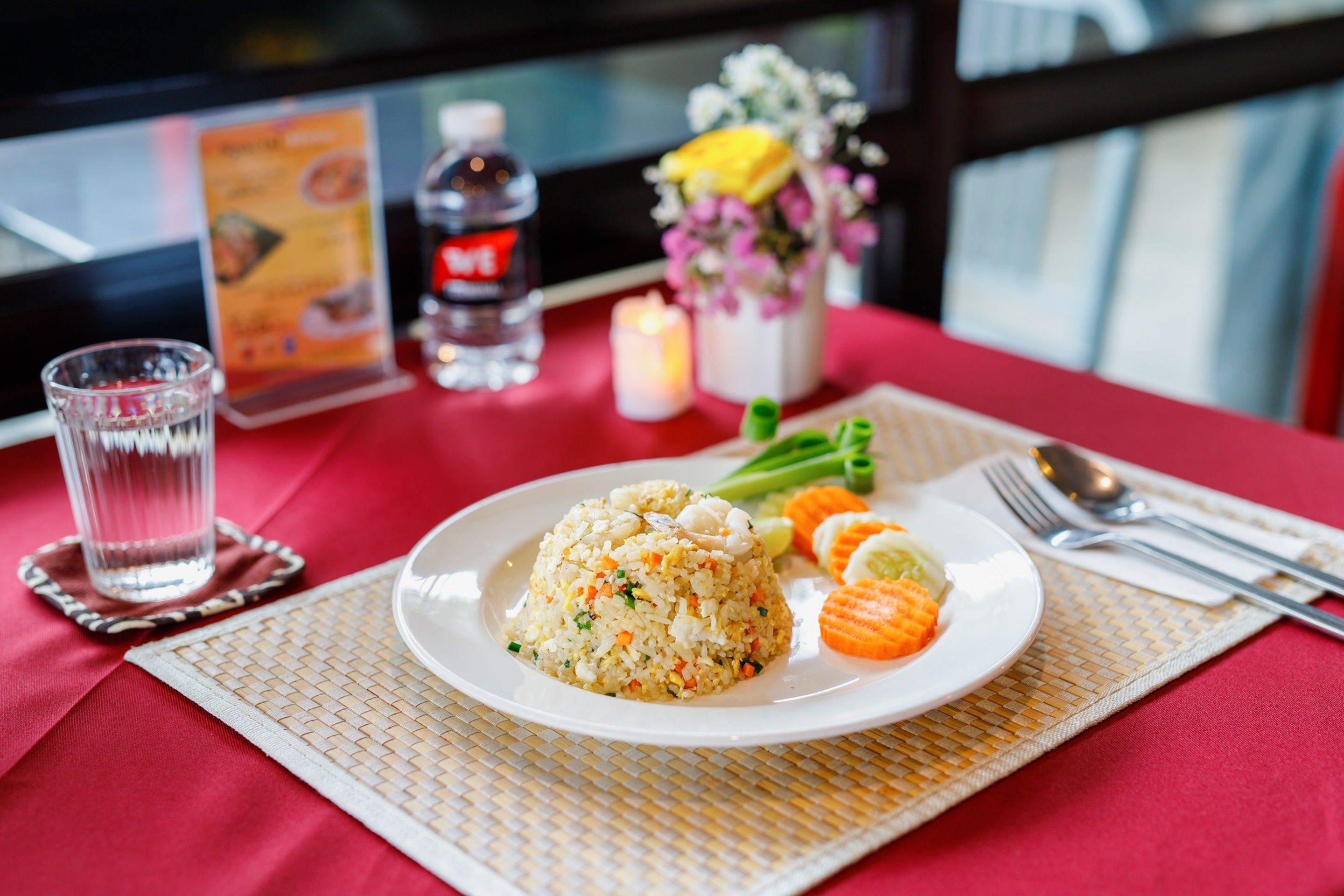Uma mesa com um prato de arroz frito, legumes e um copo de água.