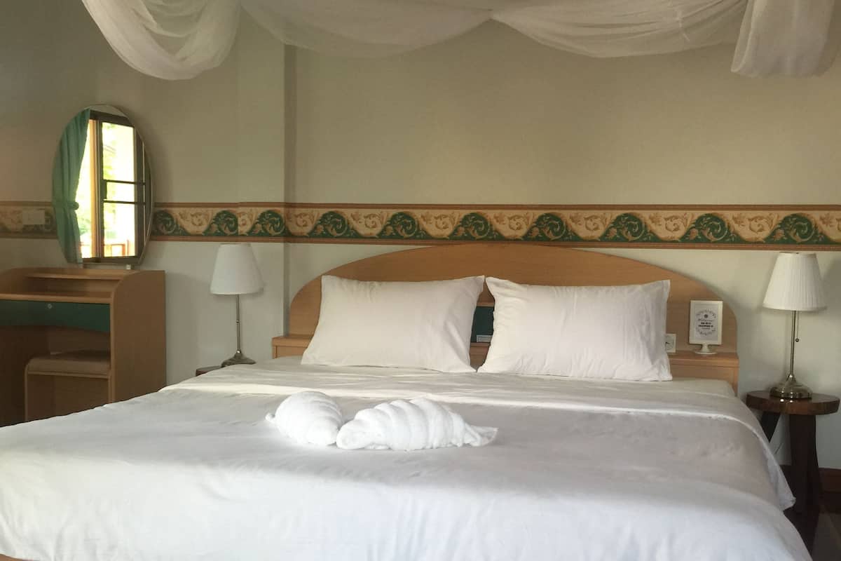 A neatly made bed with white linens and pillows, a wooden headboard, and a bedside table with a lamp.