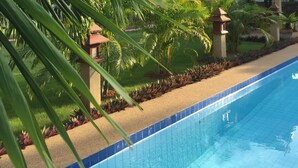 A swimming pool with a blue tiled edge, surrounded by palm trees and a building with a red roof. - Lyndale Lodge (Sam Roi Yot)