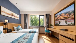 Habitación de hotel con dos camas, un escritorio, un televisor y un amplio ventanal con vistas a un edificio tradicional.