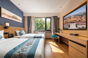 A hotel room with two beds, a desk, a TV, and a large window with a view of a traditional building.
