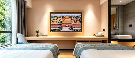 Habitación de hotel con dos camas, un escritorio con computadora, un cuadro grande de una construcción tradicional, una ventana con cortinas y un baño con espejo y lavamanos.