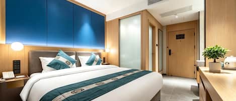 A modern hotel room with a large bed, bedside tables, a desk, and a potted plant.