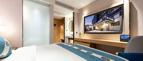 A hotel room with a bed, a desk, a television, and a view of the hotel's exterior.