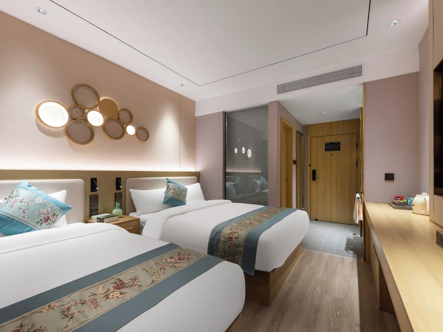 Une chambre d’hôtel avec deux lits, une télévision, un bureau et une salle de bain visible à travers une porte en verre.