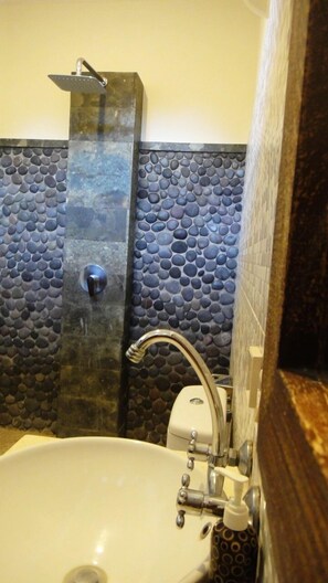 A bathroom with a stone mosaic wall, a shower, and a sink with a faucet.