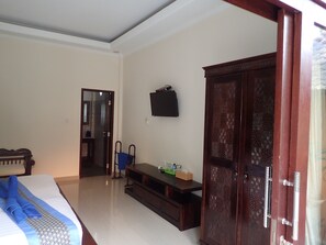 A hotel room with a bed, a wooden wardrobe, a small table with a bottle and tissues, and a TV mounted on the wall.