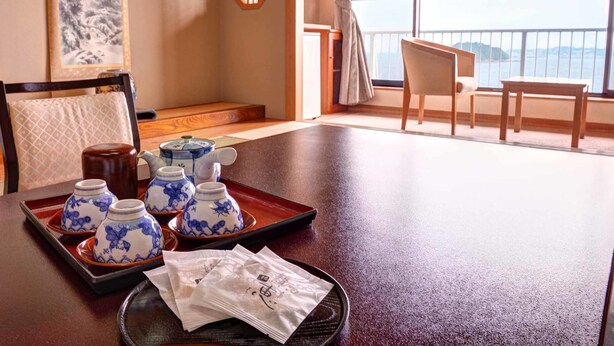 Una stanza con un tavolo da pranzo apparecchiato con teiere e tazze, una sedia e vista sul mare attraverso ampie finestre.