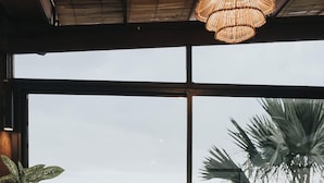 A cozy seating area with a wooden table, a cushioned bench, and a large window offering a view of tropical foliage. - MaxOne Hotels at Ubud (Ubud)