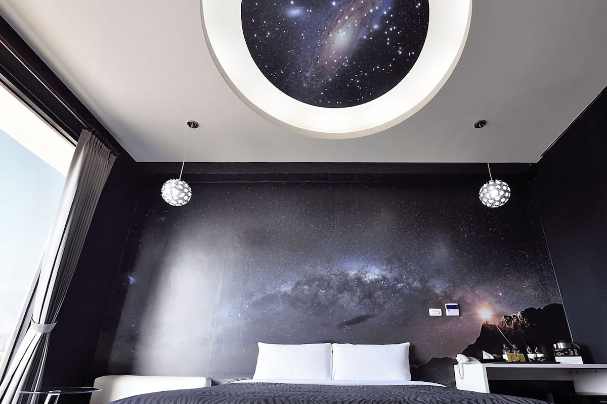A bedroom with a starry sky mural, a bed with white linens, and a round ceiling light.