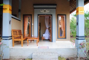 A covered outdoor seating area with wooden furniture and a bench, leading to a room with a bed and a canopy. - Tiara Homestay Pemuteran (Pemuteran)