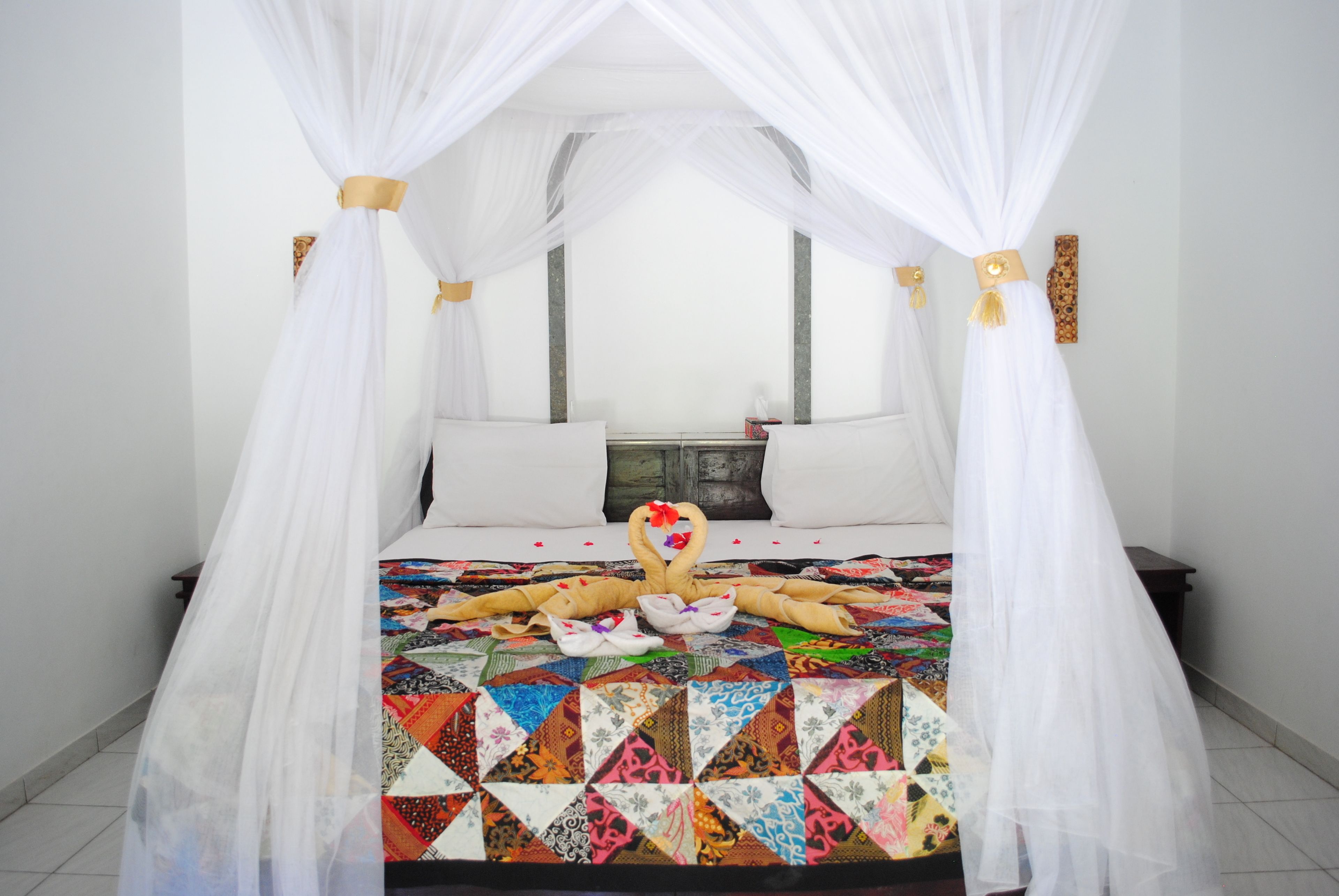 A bed with a colorful quilt, white canopy, and a decorative arrangement of towels.