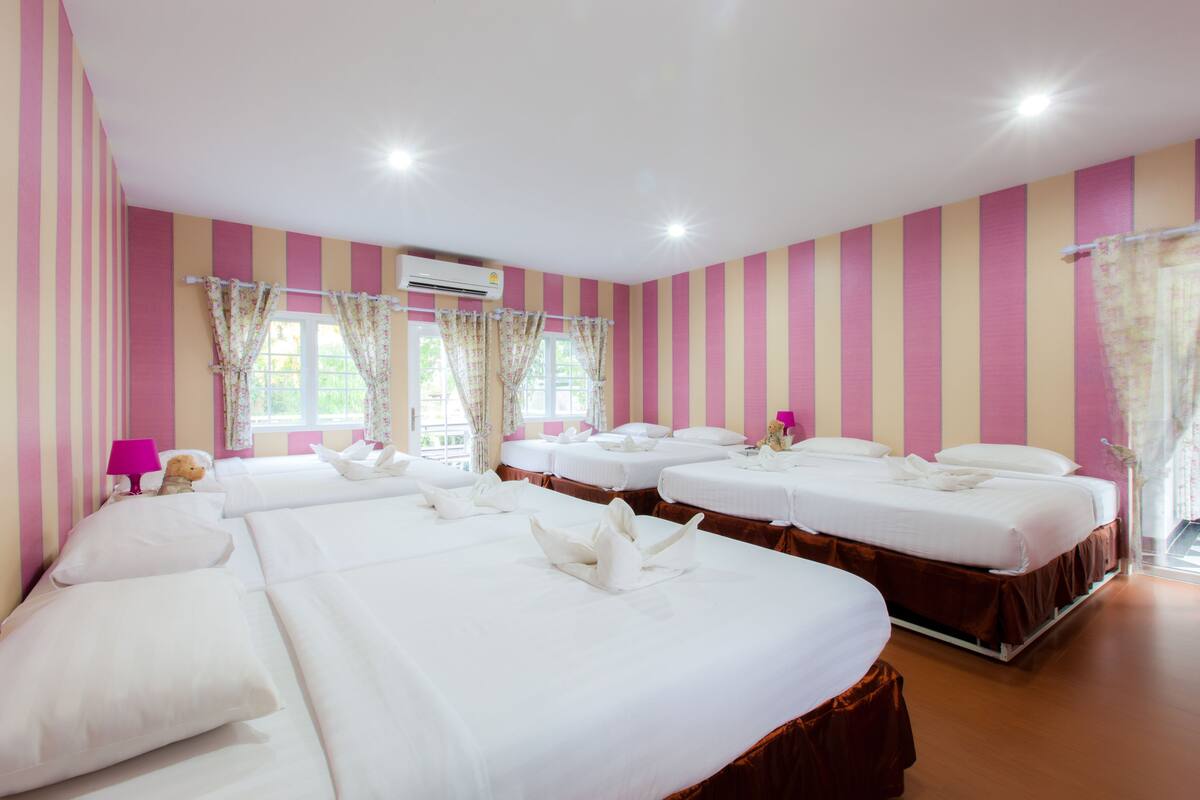A hotel room with four beds, pink and white striped walls, and a window with floral curtains.