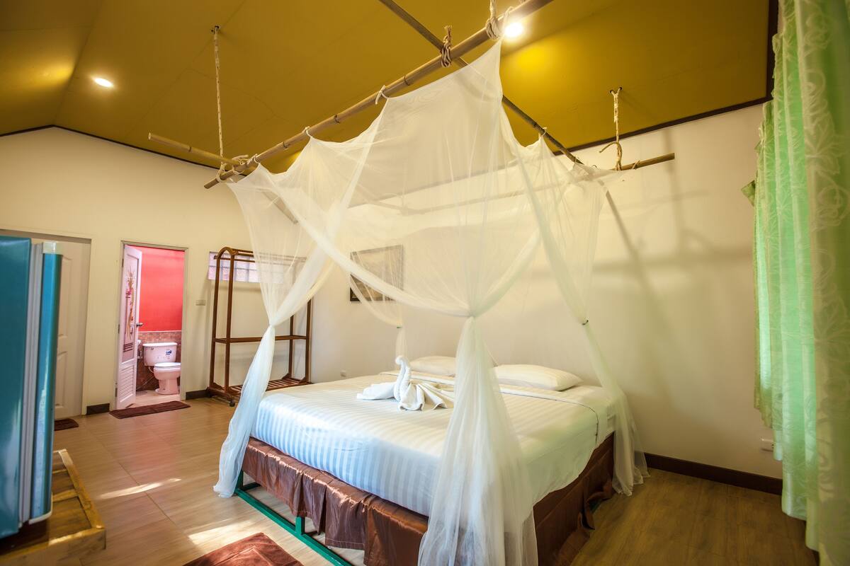 A bedroom with a four-poster bed, a wooden floor, and a visible bathroom door.